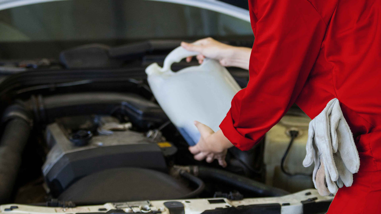 Mécanicien en combinaison rouge versant un produit dans le moteur d'une voiture, illustrant l'entretien ou le décrassage d'un moteur diesel.