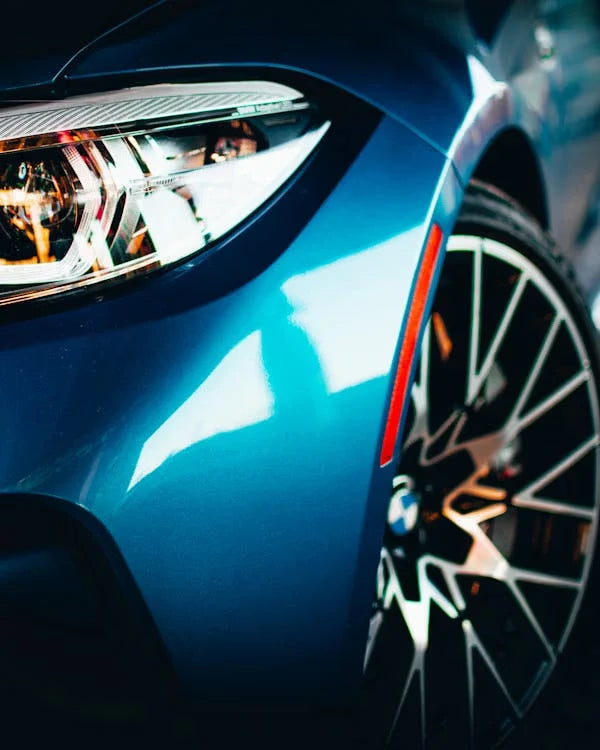 Vue rapprochée de l'avant d'une voiture BMW bleue, mettant en valeur la brillance de la carrosserie, les détails du phare et le design de la jante.